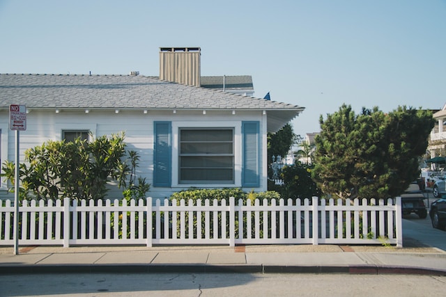 A white bungalow with blue shutters and a white picket fence