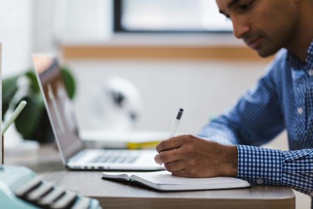 property manager writing something in a notebook with their laptop open